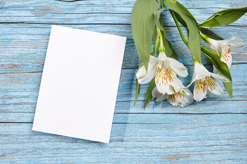White blank card mockup and alstroemeria flowers on blue wood background, top view, flat lay