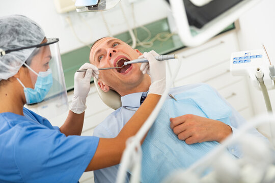 Practitioner female dentist drilling tooth to male patient businessman in dental studio