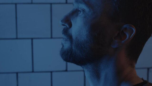 Side view of man tilting up his head and looking straight forward while standing in bunker with blue neon light
