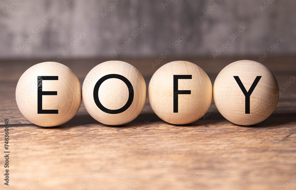 Poster selective focus. text eofy writing on block cylinder with alarm clock on a wooden background. busine