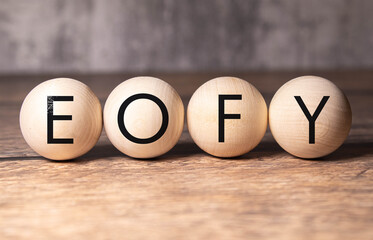 Selective focus. Text EOFY writing on block cylinder with alarm clock on a wooden background....