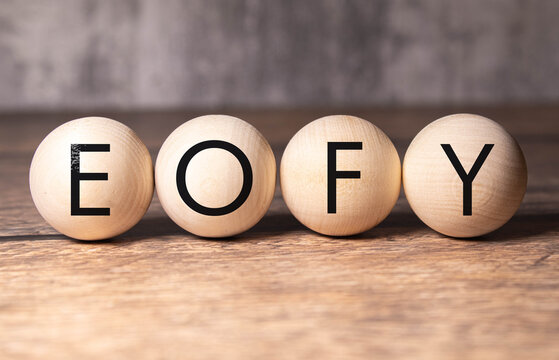Selective focus. Text EOFY writing on block cylinder with alarm clock on a wooden background. Business concept.
