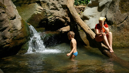 Mom with boy child in tropical waterfall. Creative. Family of hikers on a summer trip in jungles.