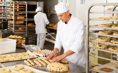man in chefs uniform kneading dough in bakery