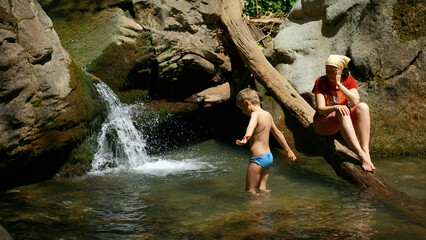 Mom with boy child in tropical waterfall. Creative. Family of hikers on a summer trip in jungles.