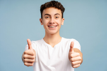 Portrait of smiling boy, teenager with dental braces showing thumbs up looking at camera