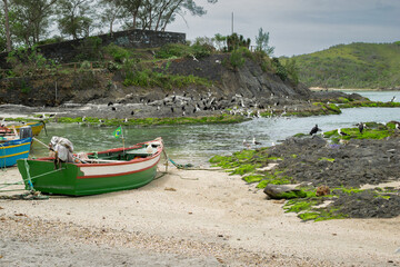 Large beach stones at Forte São Mateus in Cabo Frio, with sea water around it, many fishing boats and many birds on the stones.