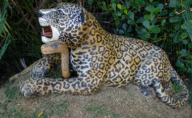 Life-size wooden sculpture of a jaguar, displayed in a park.