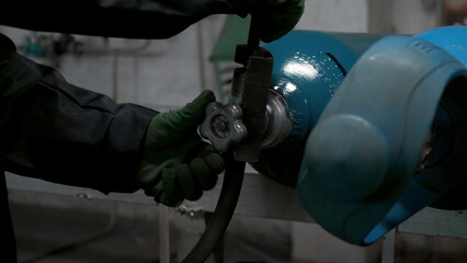 Close up of worker in gloves turning gas cylinder valve. Clip. Industrial background of the factory.