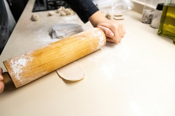 A boy, using a rolling pin to flatten dough on a kitchen counter.
