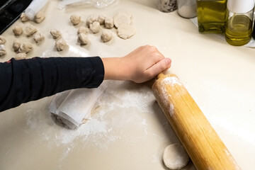 A person is kneading dough on a counter, with a boy using a rolling pin in the background.