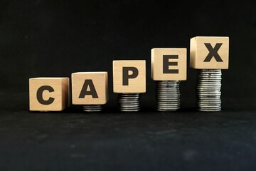 Increase in capex or capital expenditure concept. Wooden blocks with increasing stack of coins in black background. - obrazy, fototapety, plakaty
