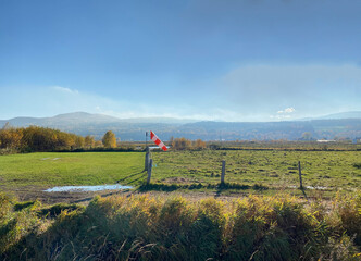 Orange and white windsock in a field. Flag on a mast to indicate wind direction and speed for a...
