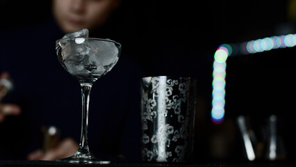 Close up of glass with ice cubes prepared for cocktail. Media. Bartender mixing alcohol liquids in a shaker.