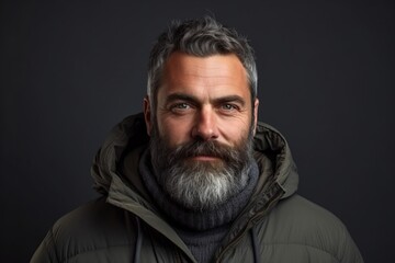 Portrait of a handsome bearded man with gray beard and mustache wearing warm jacket on dark background