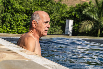 Adult male with gray hair swimming calmly in pool in summer. Lifestyle.