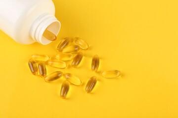 White medical bottle and vitamin capsules on yellow background, above view. Space for text