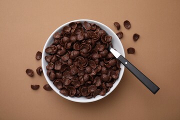 Breakfast cereal. Chocolate corn flakes in bowl and spoon on brown table, top view