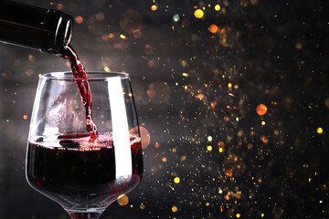 Pouring red wine into glass against dark background with blurred lights, closeup. Space for text