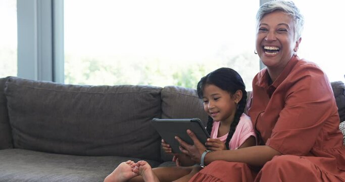 Biracial grandmother and her granddaughter are sharing joyful moment with tablet, with copy space