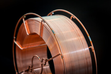 Coil of copper wire on a dark background. Shiny copper wire wound on a reel, dark background, close-up. Electronics and industrial equipment