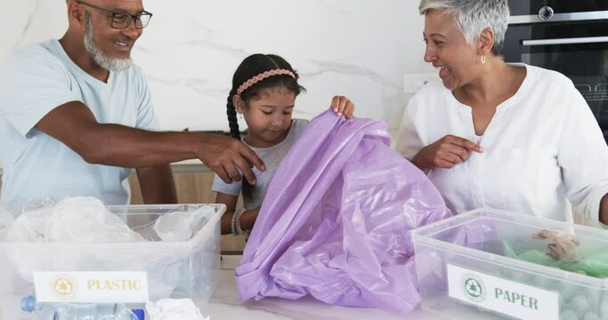 Biracial family sorts recycling, with a granddaughter placing plastic in a bin