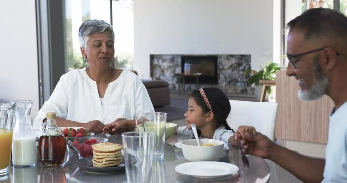 Biracial grandparents enjoy breakfast with their young granddaughter, surrounded by pancakes and fru