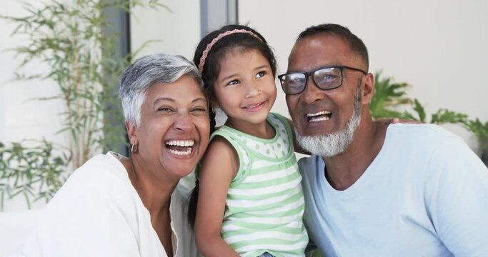 Biracial girl with a beaming smile is flanked by her joyful grandparents