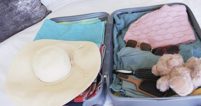 A suitcase is open, revealing neatly packed clothes and a teddy bear