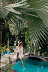 Woman have a rest and chill in the pool with amazing view on the jungle sit on the wooden bridge and look on blue water of swimming pool