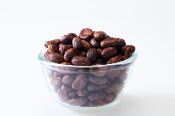 Roasted cocoa beans in a glass bowl on white