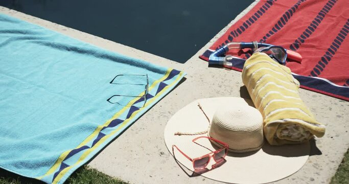 Sunglasses, a hat, and towels are beside a pool, suggesting a leisurely day