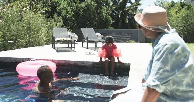 Biracial family enjoys a sunny day by the pool, with a child ready to jump in