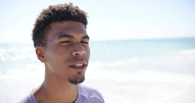 A young biracial man smiles brightly at the beach with copy space