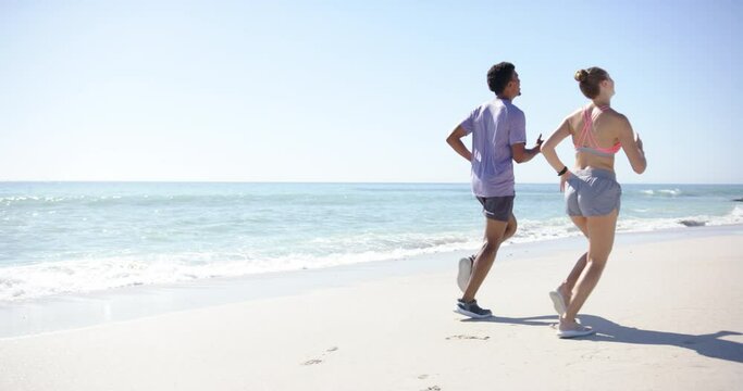 Young biracial man and Caucasian woman are jogging on a sunny beach with copy space