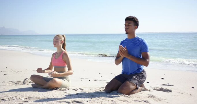 A man and woman are meditating on a sunny beach with clear skies
