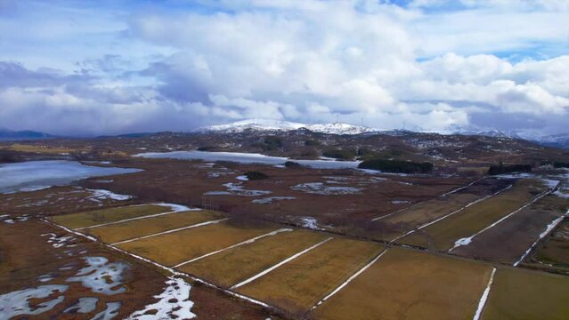 Wide dolly forward aerial view of wind turbines on snow covered hills in Sortland Norway, with farm fields in the foreground