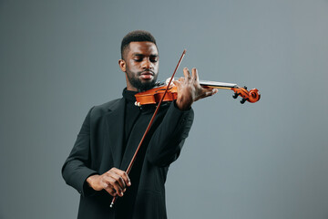 Talented African American man in a suit playing the violin with passion on a gray background - obrazy, fototapety, plakaty