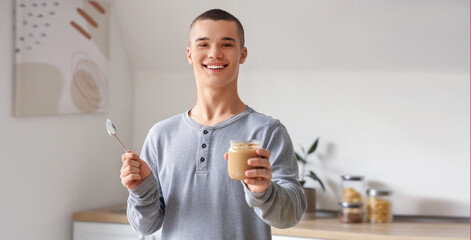 Happy young man with tasty nut butter in kitchen