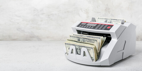 Modern cash counting machine with dollar banknotes on light background