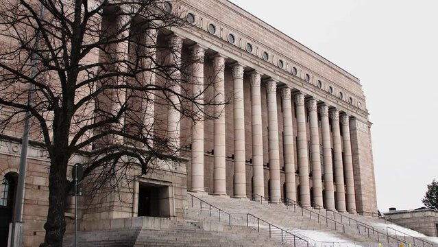 Tree branches framing the imposing facade of Helsinki's Parliament House, overcast sky