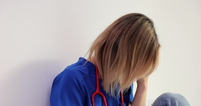 Healthcare stress and sad nurse with burnout sitting in corrido
