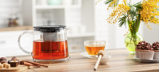 Teapot and cup of black tea with sweets and honey on table in kitchen