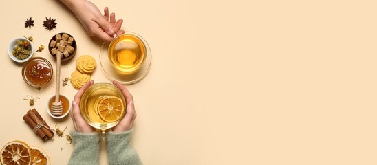 Female hands with glass cups of hot tea with citrus fruit, sugar, spices and cookie on beige background with space for text