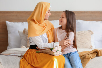 Little girl and her Muslim mom with tulips hugging in bedroom on Mother's Day