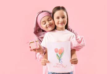 Little girl with greeting card and gift for her Muslim mother on pink background