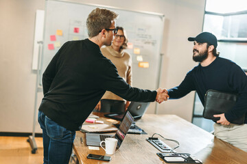 Successful partnership: Business men shaking hands in a creative tech company