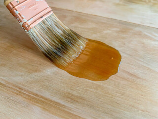 Close-up shot of a paintbrush brushing in polyurethane on a wood plank