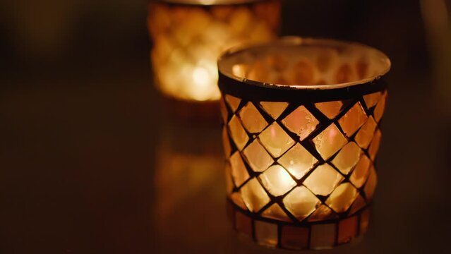 Pair of glass candles with a lattice diamond design softly glowing in the dark, radiating warmth and tranquility. Static shot.