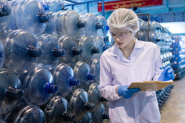 Female worker using tablet checking quality drinking water before process of filling water into...